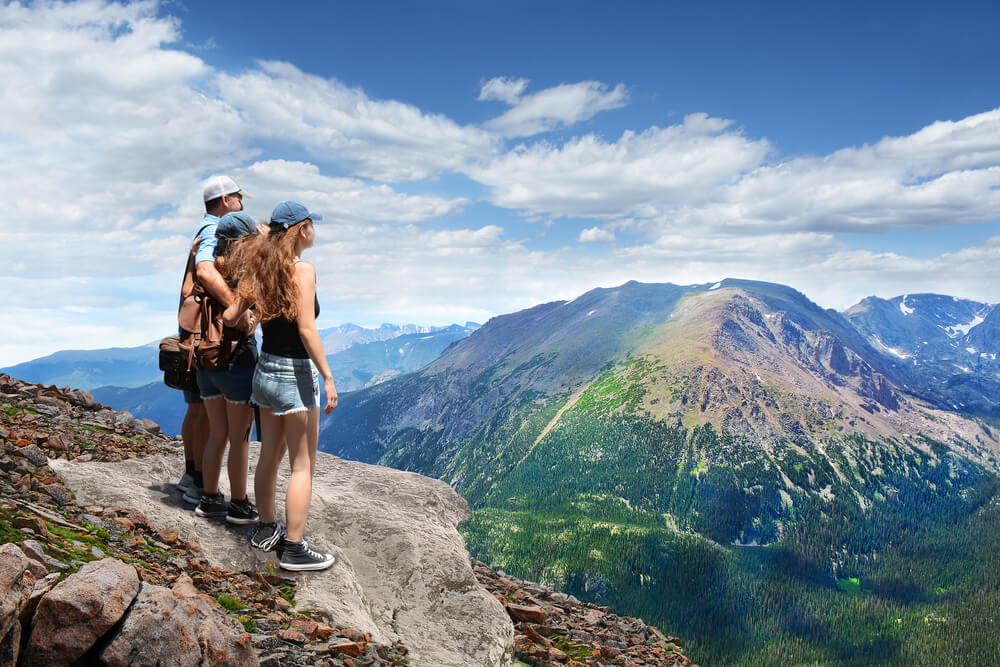 Father with arms around his family looking at summer mountains